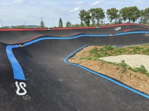 Virage relevé de pumptrack avec marquage directionnel bleu et rouge pour guider les usagers.