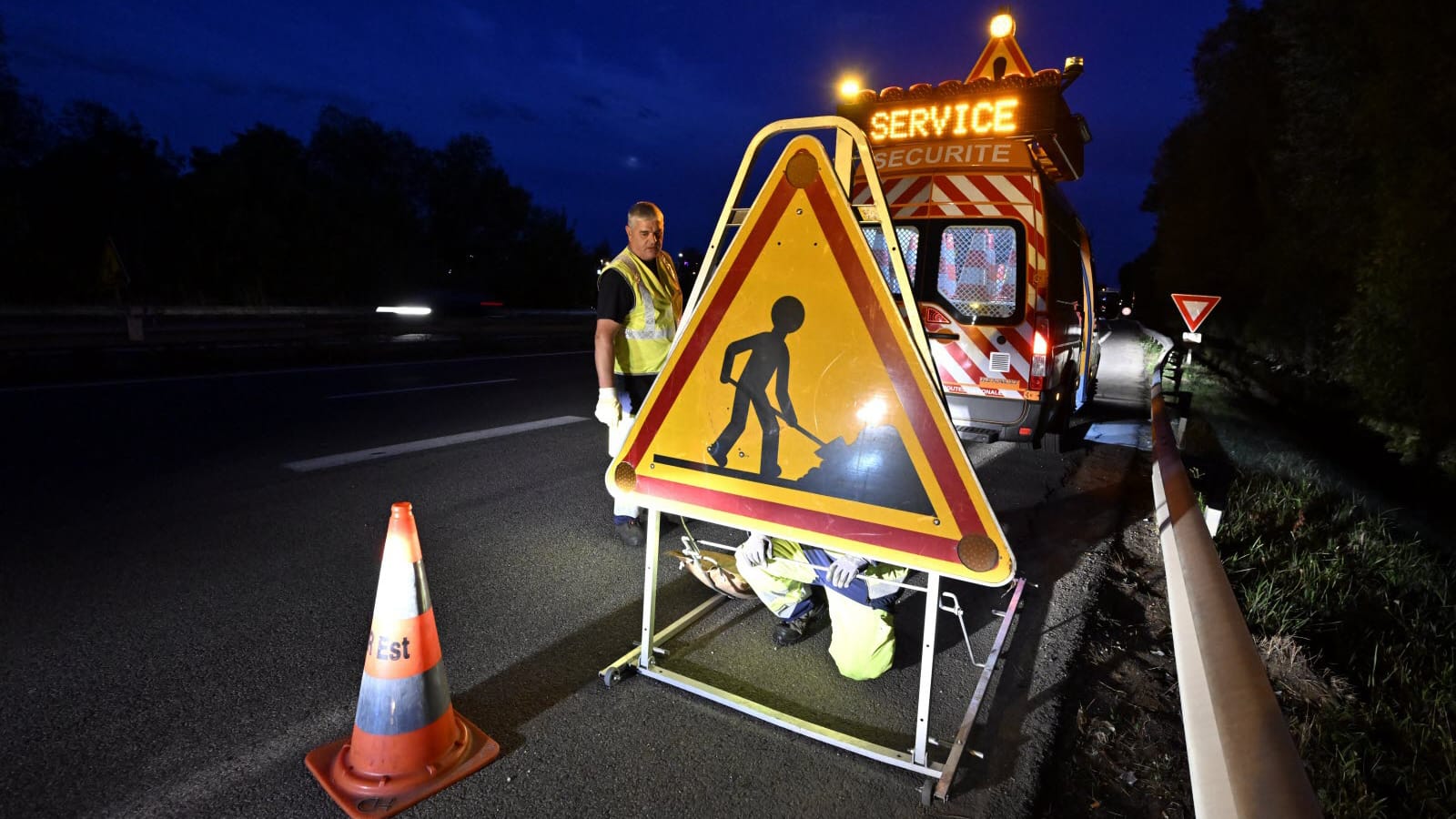 Agent de la DIR Est en gilet haute-visibilité installant un panneau de chantier triangulaire AK5 de nuit sur l'autoroute A33