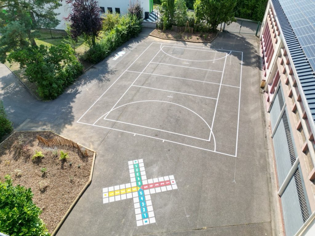 Vue drone d'une cour d'école avec terrain sportif coloré et marelle chiffres au sol à Hargarten-aux-Mines