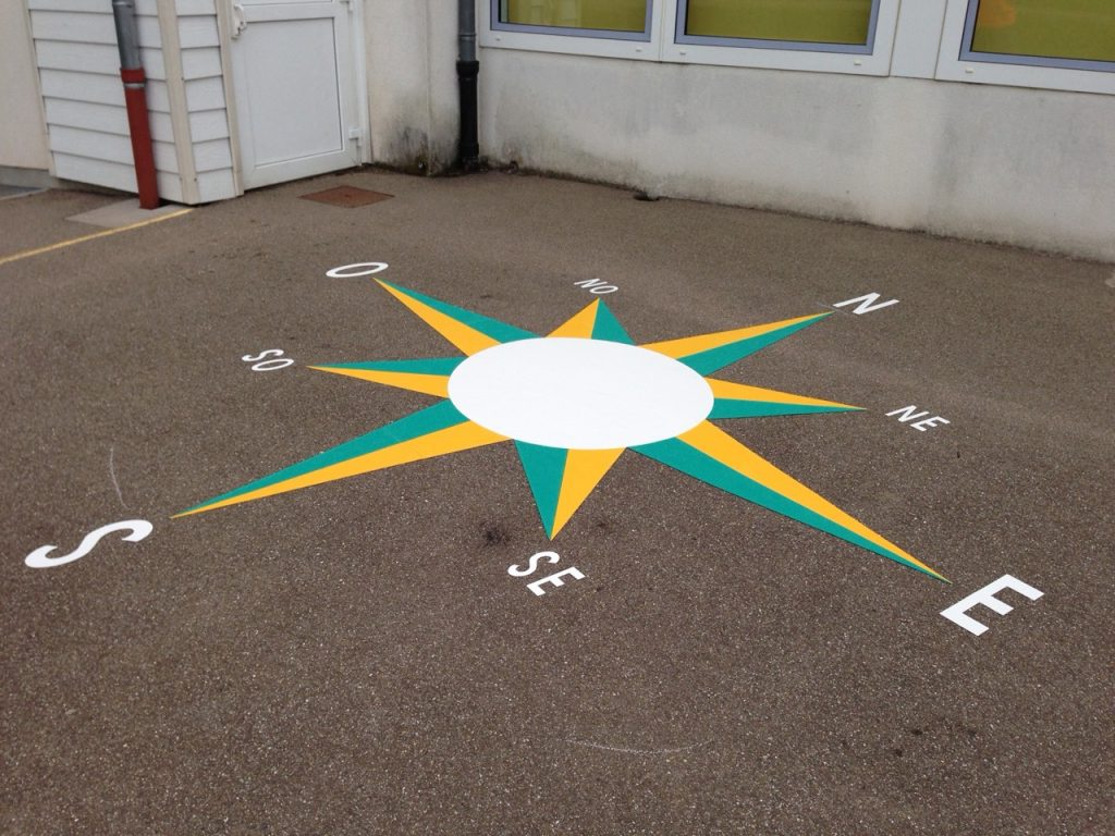 Rose des vents jaune et verte avec points cardinaux peinte au sol d'une cour d'école pour l'apprentissage de la géographie