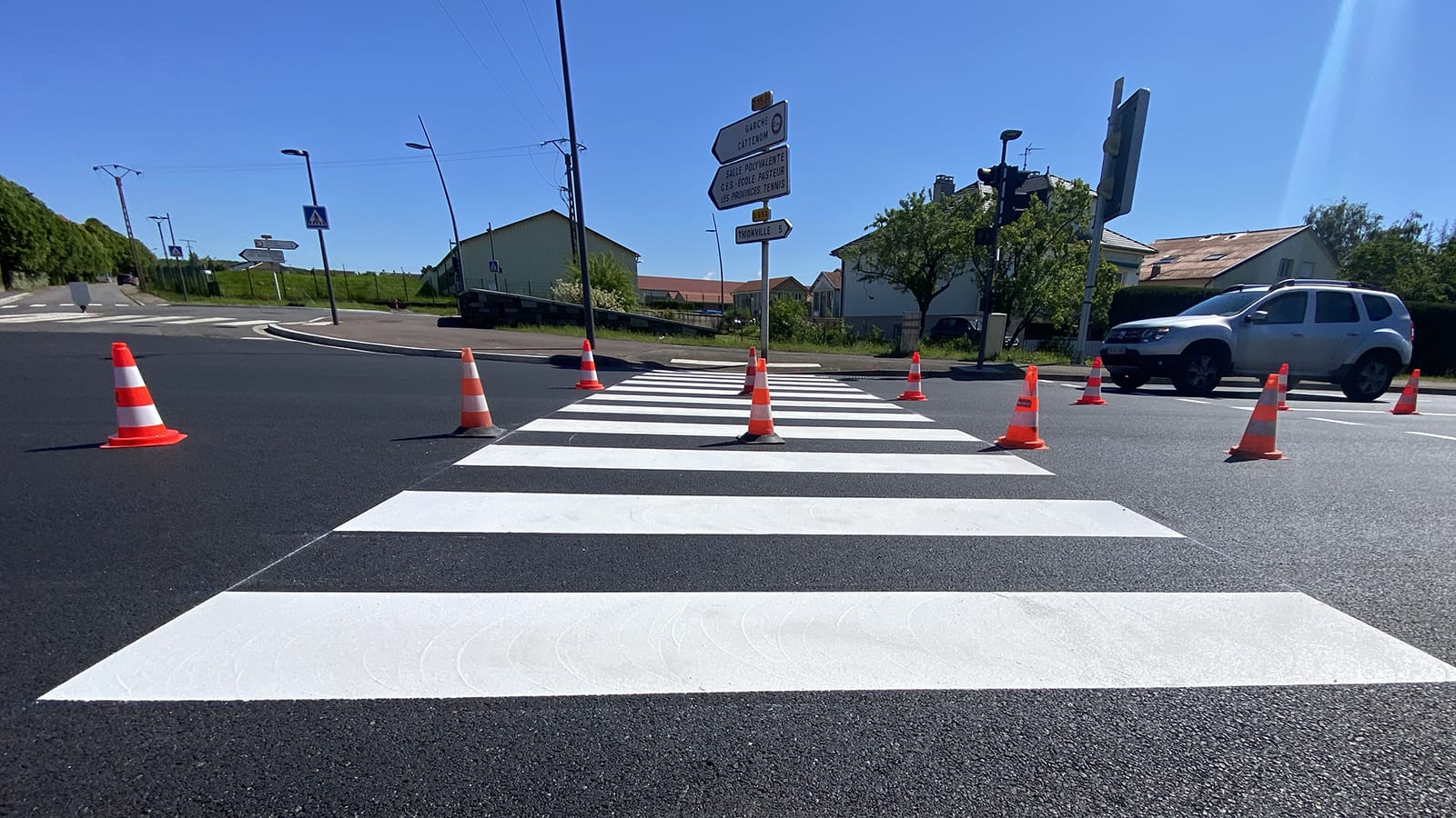 Passage piéton fraîchement marqué en enduit à froid blanc résinolé avec cônes de signalisation oranges en cours de séchage