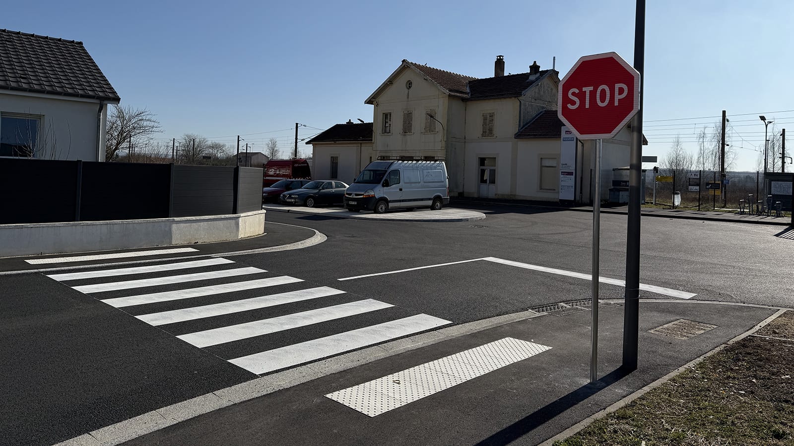 Passage piéton fraîchement marqué avec bandes blanches, panneau STOP en bordure et dalles podotactiles PMR devant une gare