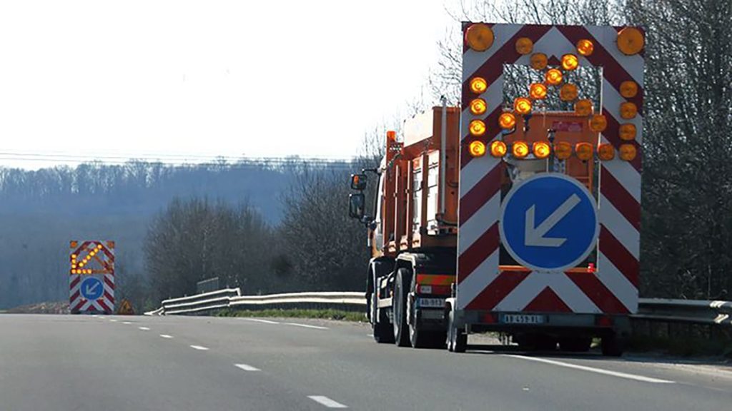 Camion équipé d'une flèche lumineuse orange avec panneau directionnel, assurant la protection d'un chantier mobile sur route départementale