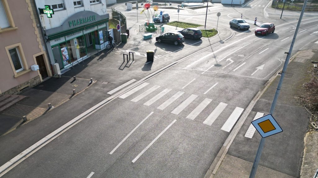 Vue aérienne prise par drone d'un passage piéton en zone urbaine avec pharmacie, devant une intersection traversante