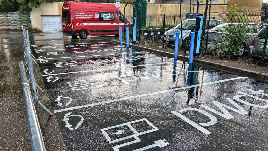 Pictogramme véhicule électrique peint au sol sur fond vert d'une place de recharge