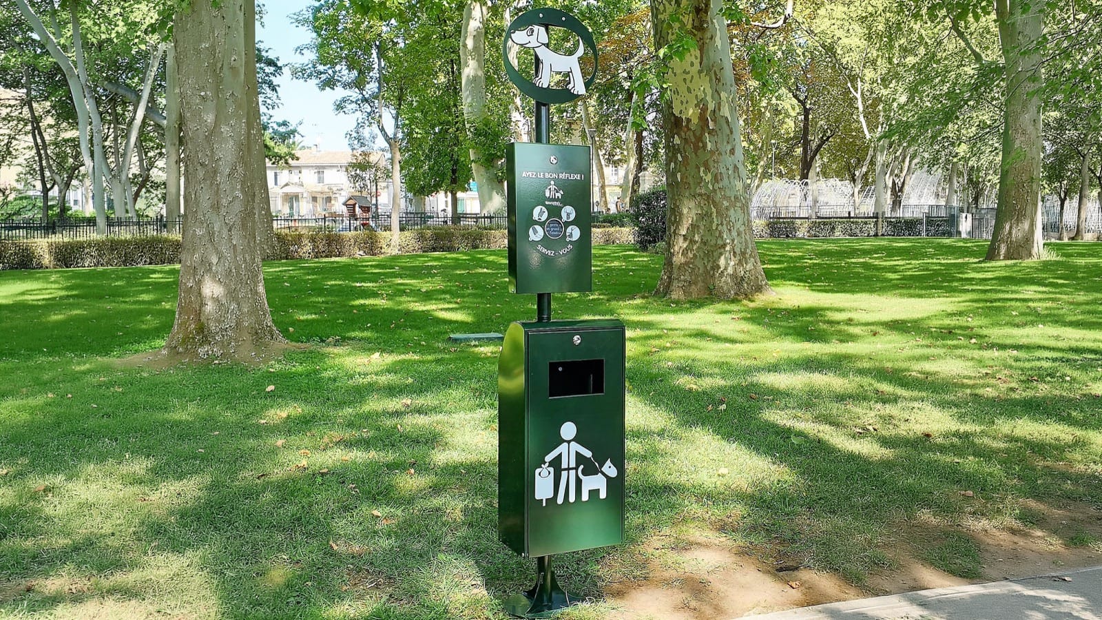 Borne de propreté canine installée dans un parc avec distributeur de sacs et corbeille