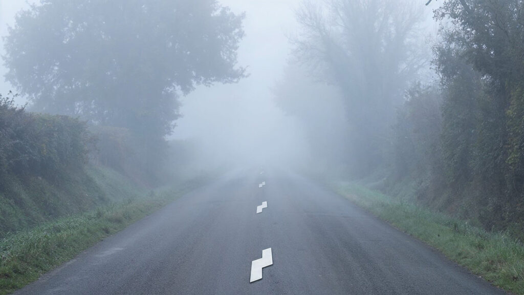 Route étroite balisée par des modules MRE dans le brouillard