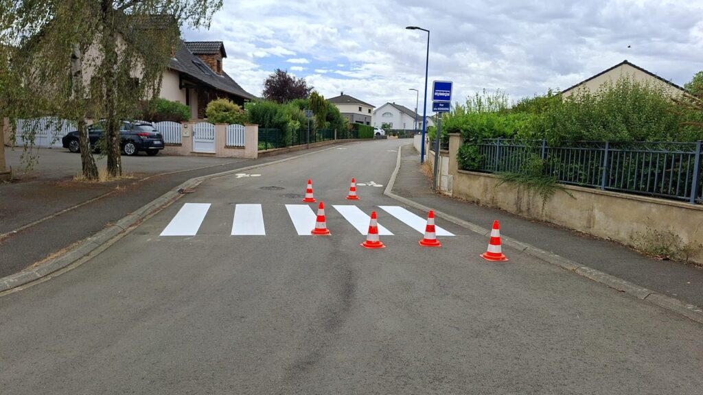 Passage piéton fraîchement marqué et protégé par des cônes, en demi-chaussée sous circulation alternée.