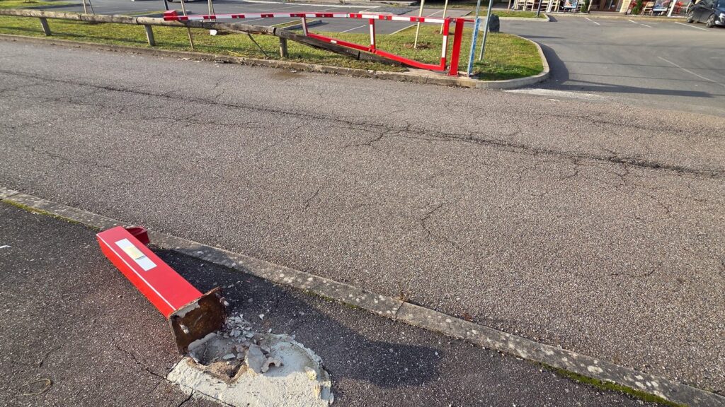 Ancienne barrière de parking accidentée avec support arraché de son massif béton