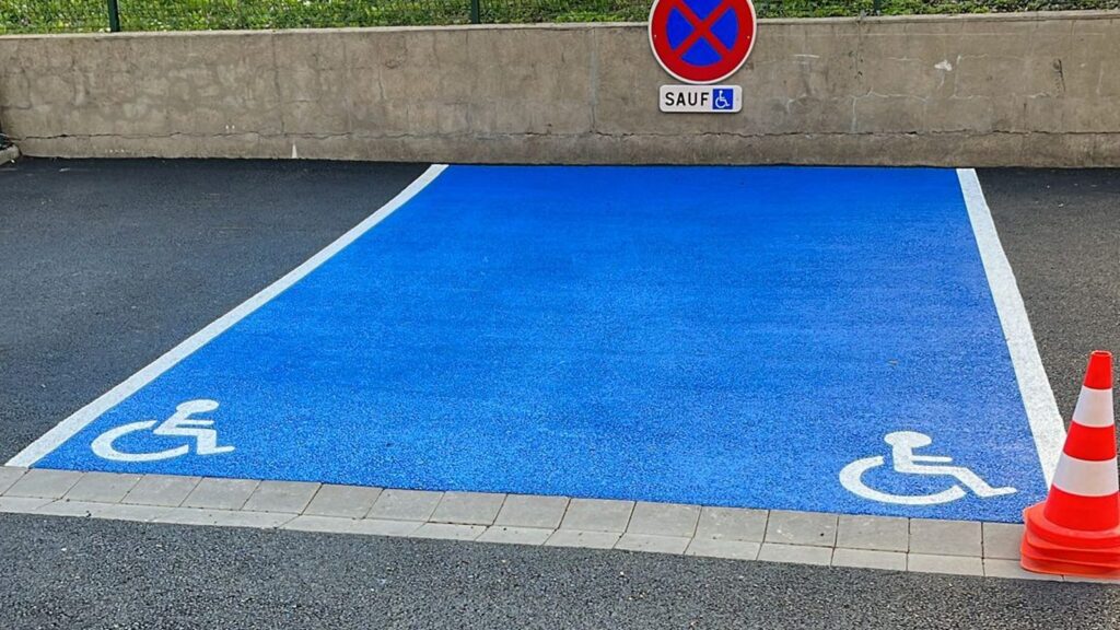 Place PMR bleue avec pictogrammes blancs et signalisation verticale dans le parking d'une copropriété